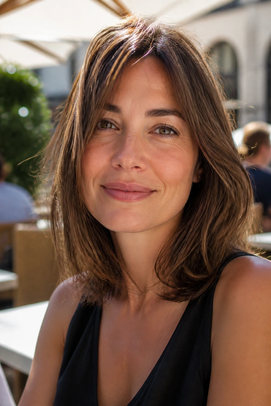 Real woman with airy shoulder-length bob in sunny outdoor cafe setting