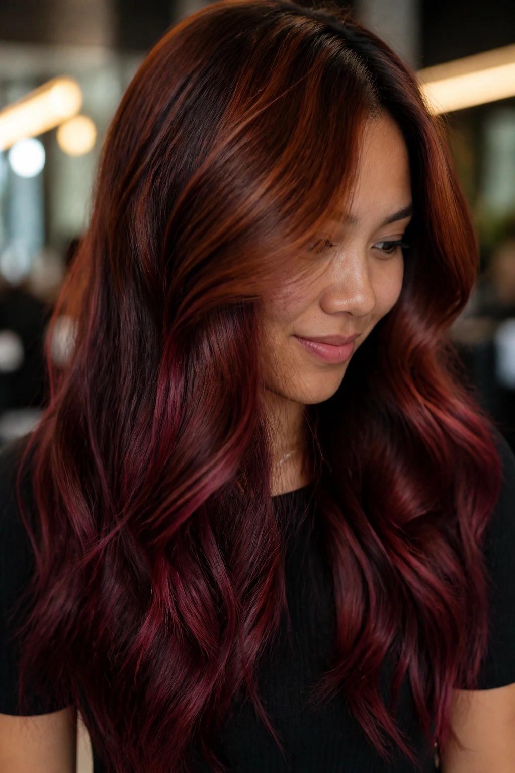 Close-up portrait of a real person with an auburn-to-burgundy hair melt in warm salon lighting