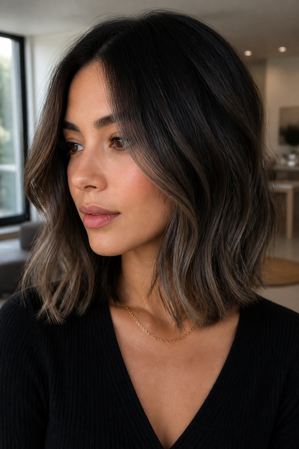 Portrait of a woman with mushroom brown balayage on a black lob in soft daylight.