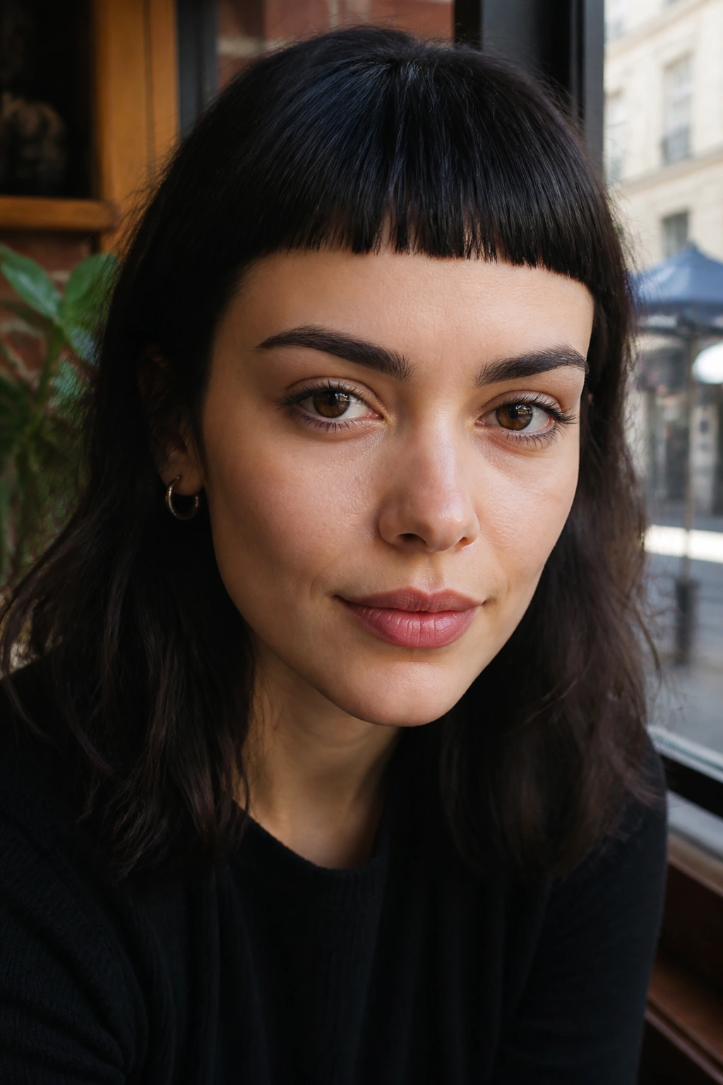 Close-up of a real woman with sharp blunt micro bangs in a cafe setting