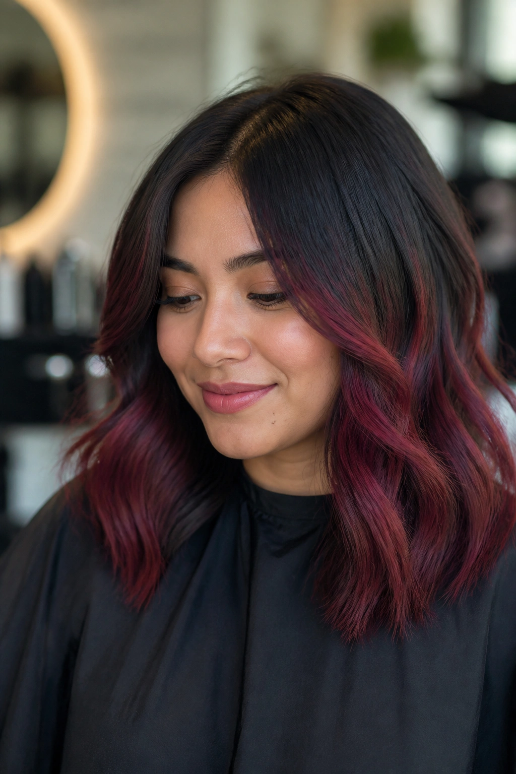Close-up of a real woman with burgundy balayage starting at mid-lengths on black hair