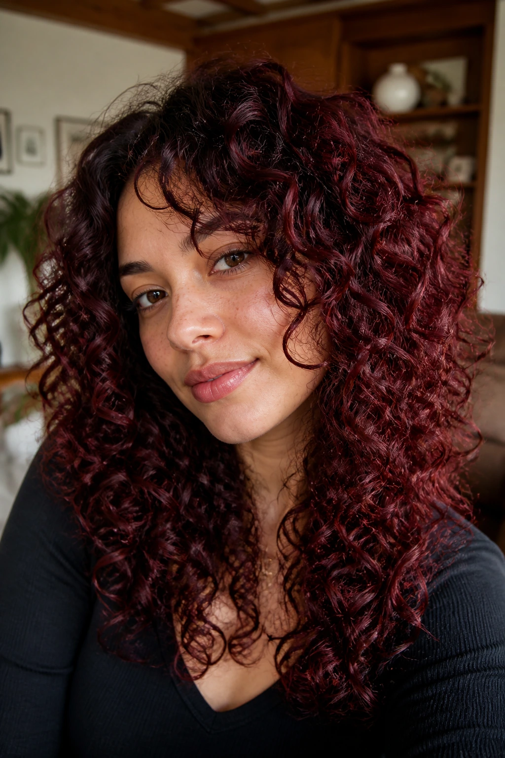 Close-up of burgundy curly layered hair on a real woman in warm interior light
