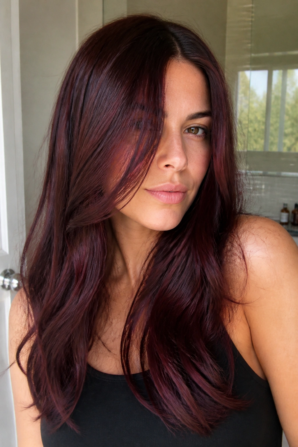 Close-up of a real woman with burgundy gloss over brunette hair in bright daylight