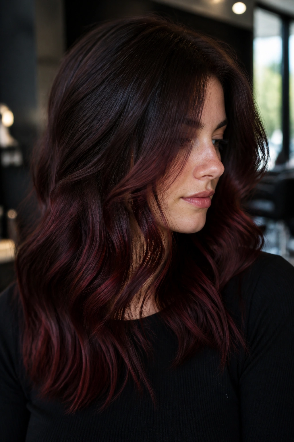 Brunette with burgundy shadow balayage in moody salon lighting