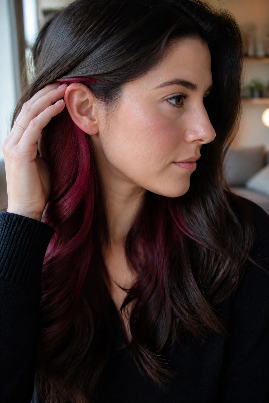 Close-up of brunette with burgundy underlayer visible behind ear in warm indoor light