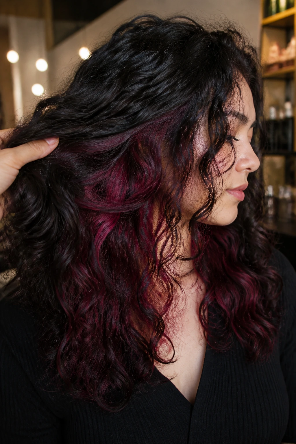 Close-up head and shoulders of a person with burgundy underlayers visible under black hair