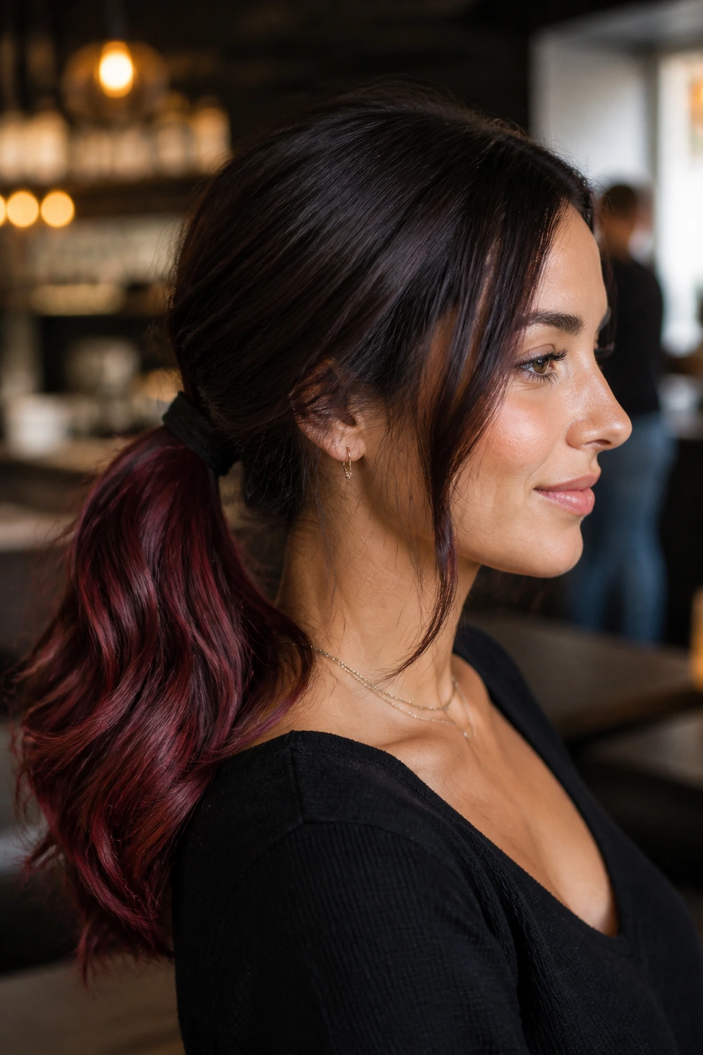 Close-up portrait of a real woman showing burgundy ends on dark brown hair in a low ponytail.