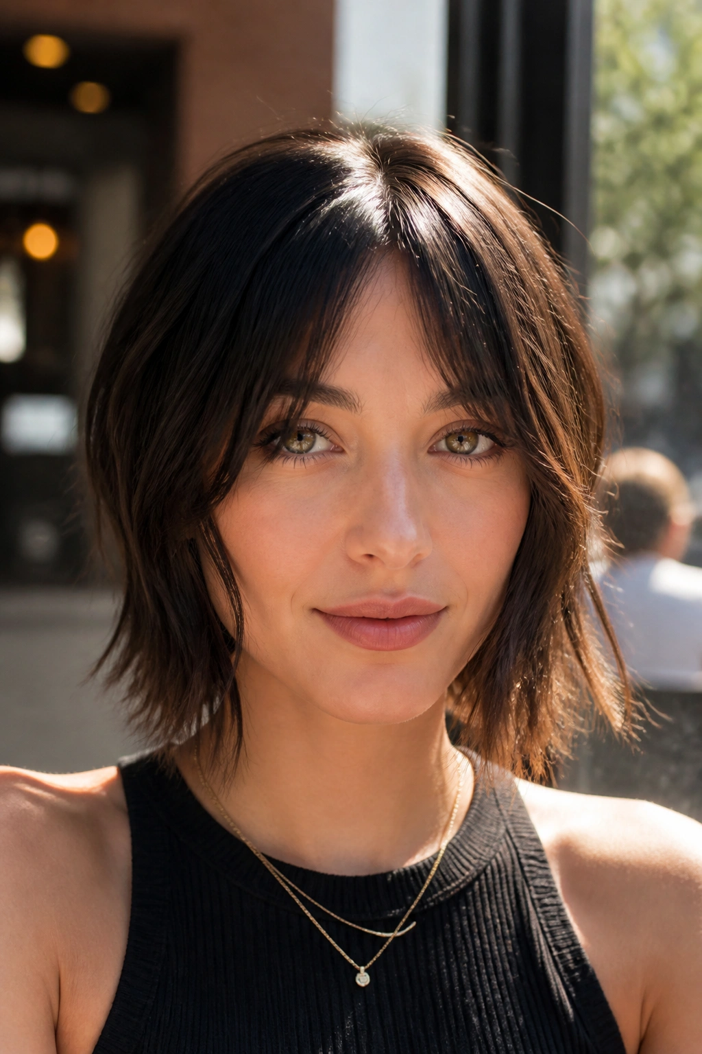 Close-up of a woman with center-part choppy bangs and face-framing ends in cafe light