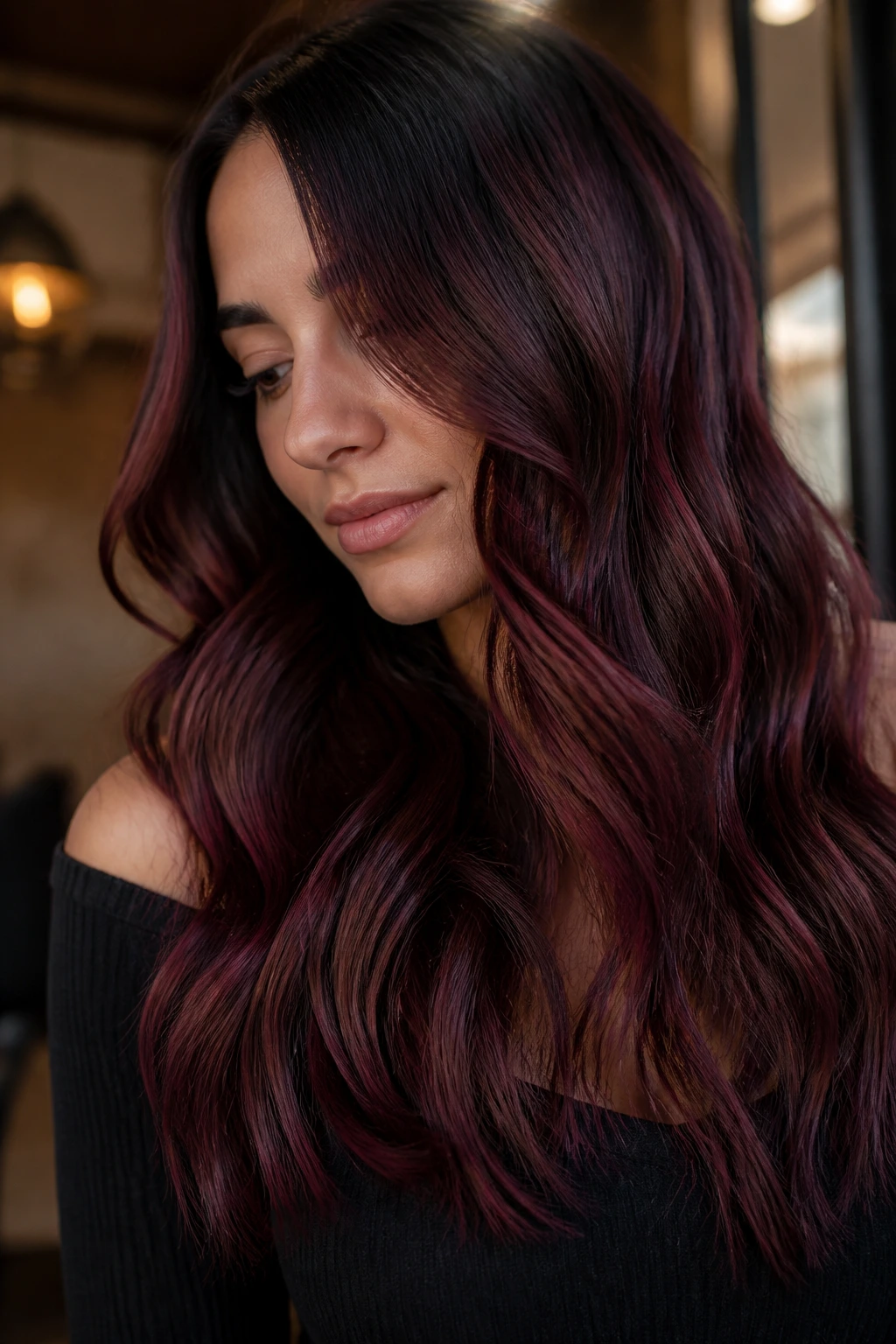 Close-up of a real woman's dark wavy hair with chocolate cherry balayage under warm indoor light