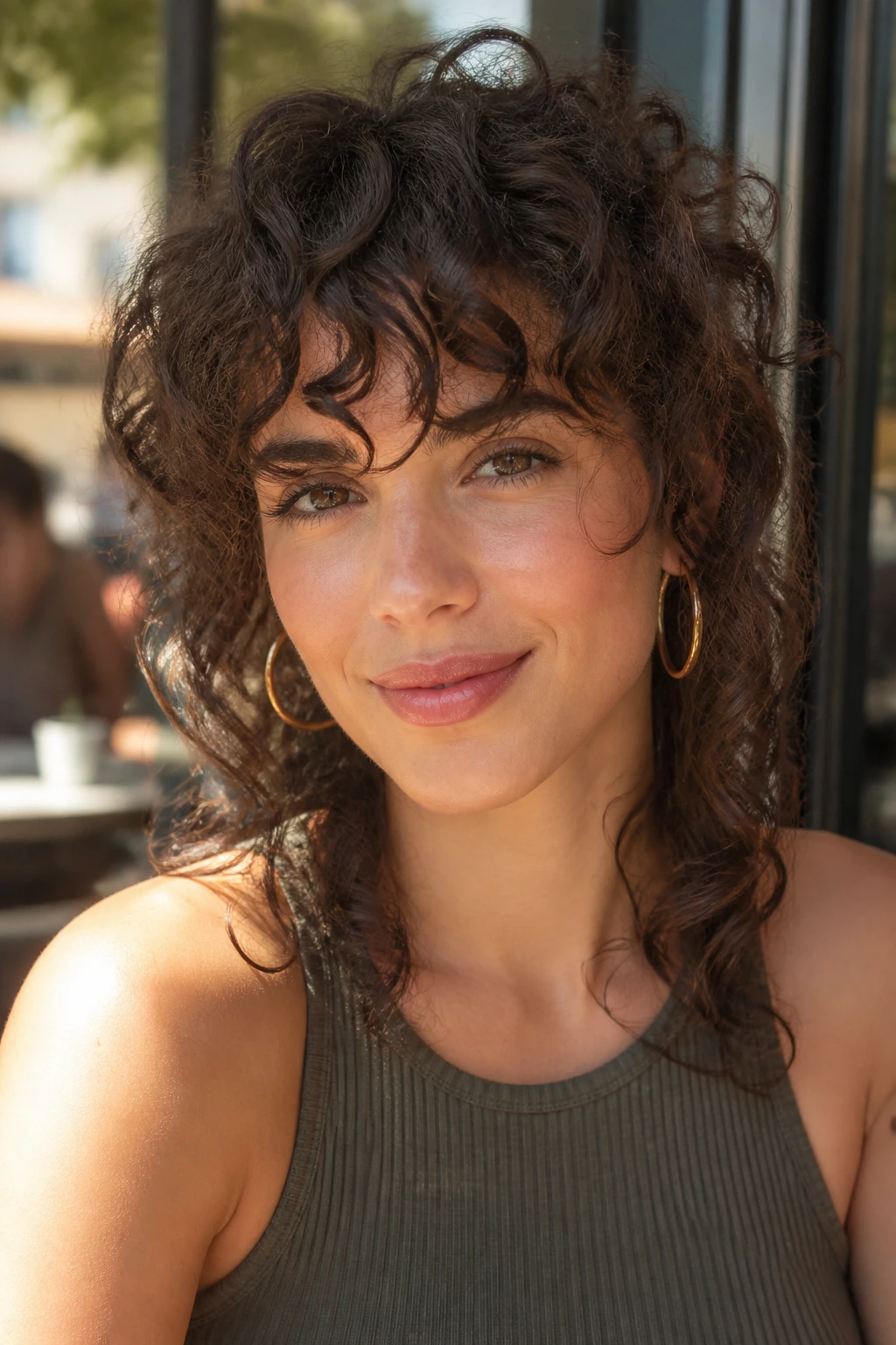 Close-up of a real woman with curly, choppy bangs in a sunlit cafe setting