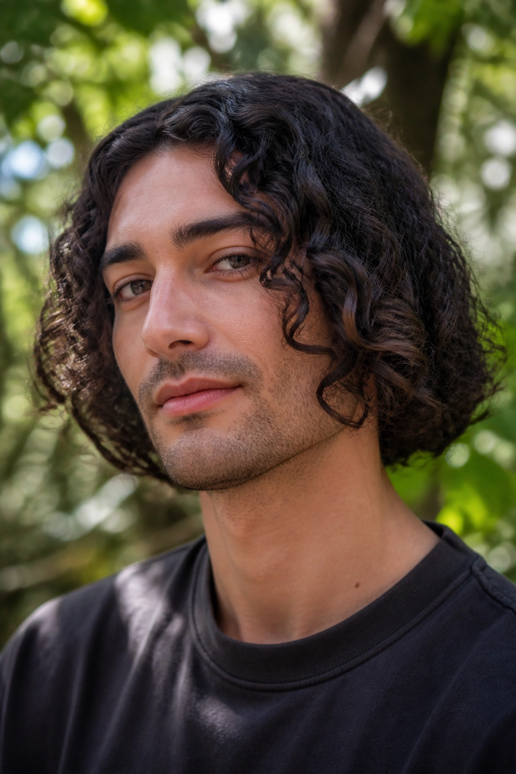 Close-up of a man with a curly bob hairstyle, curls framing the jawline.