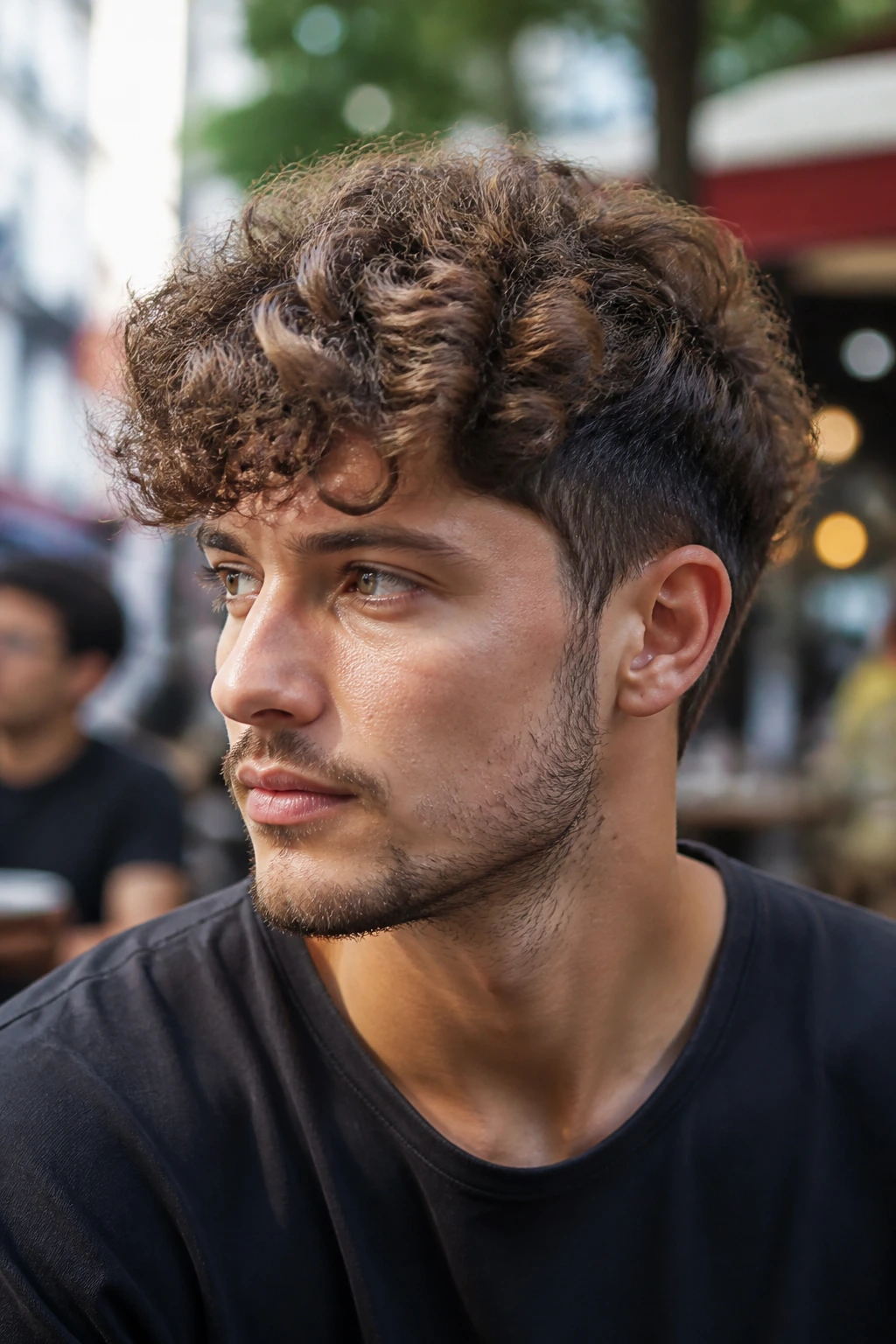 Close-up of a man with a curly medium crop hairstyle in outdoor cafe light