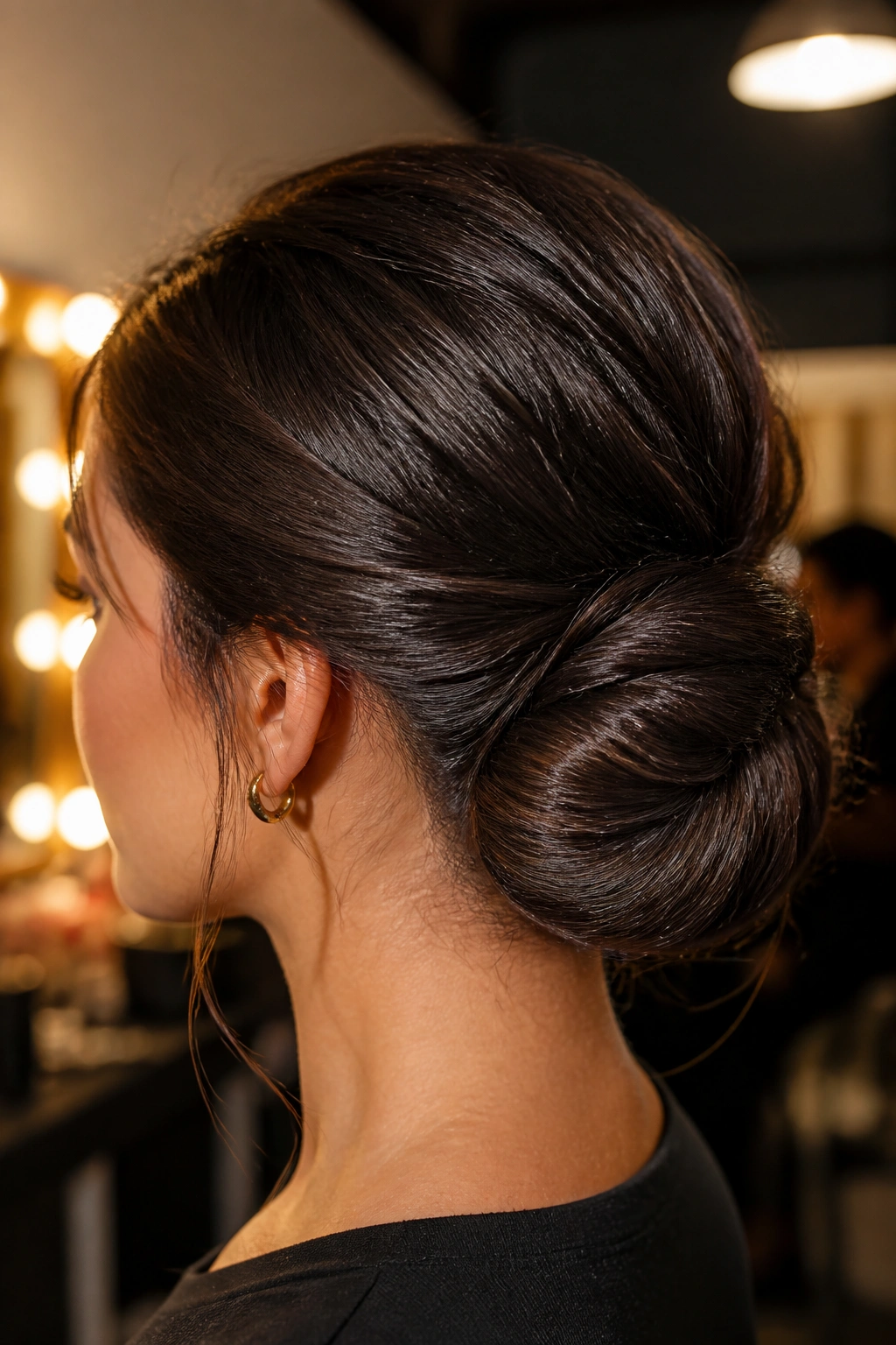 Close-up of a real person with a folded low bun for thick long hair, backstage lighting