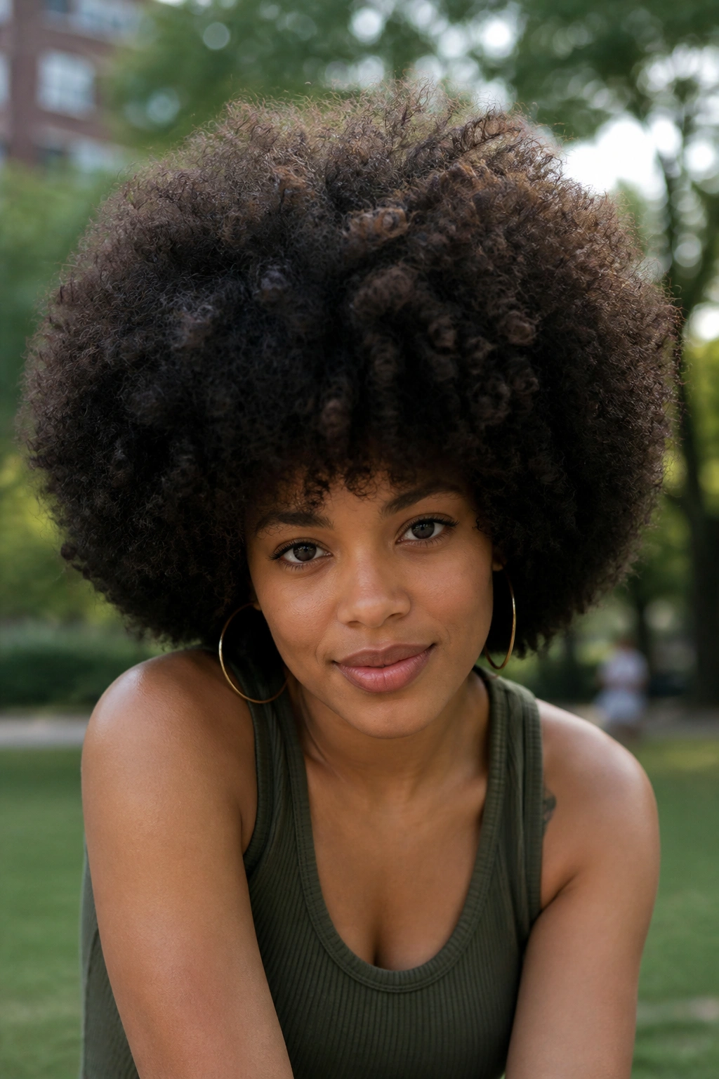 Close-up portrait of a real woman with a dense, spherical full rounded Afro in an outdoor setting.
