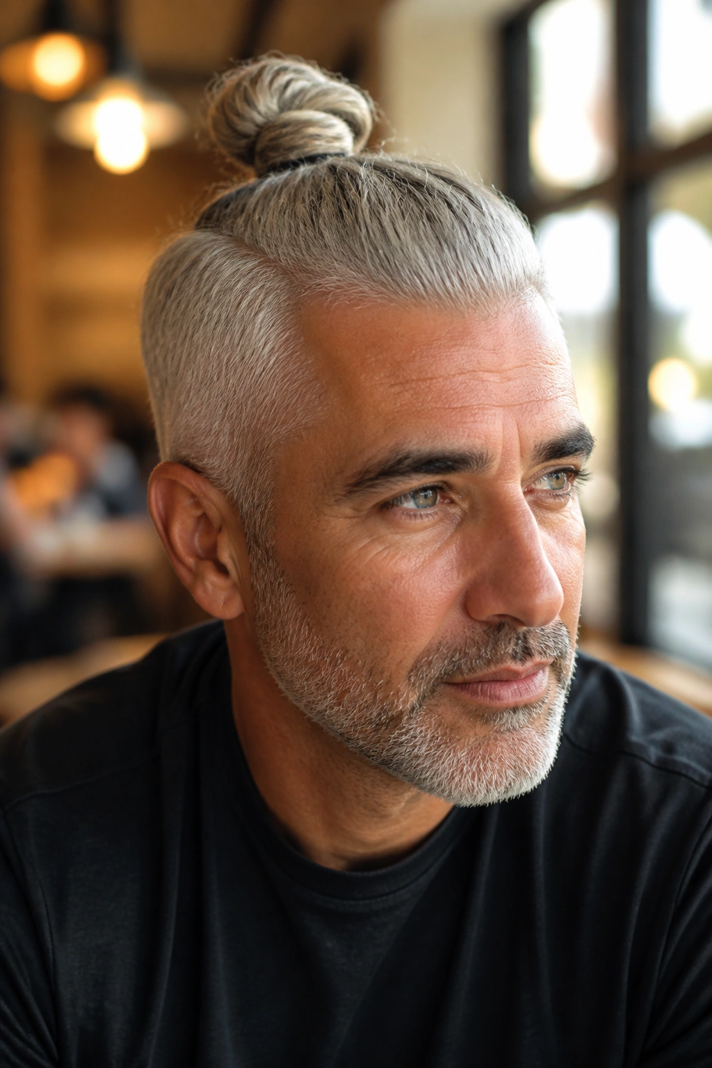 Close-up portrait of a man with a grey top knot in a cafe light.