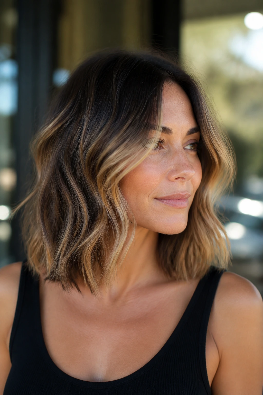 Close-up of a woman with a wavy lob featuring honey balayage from cheekbone to ends
