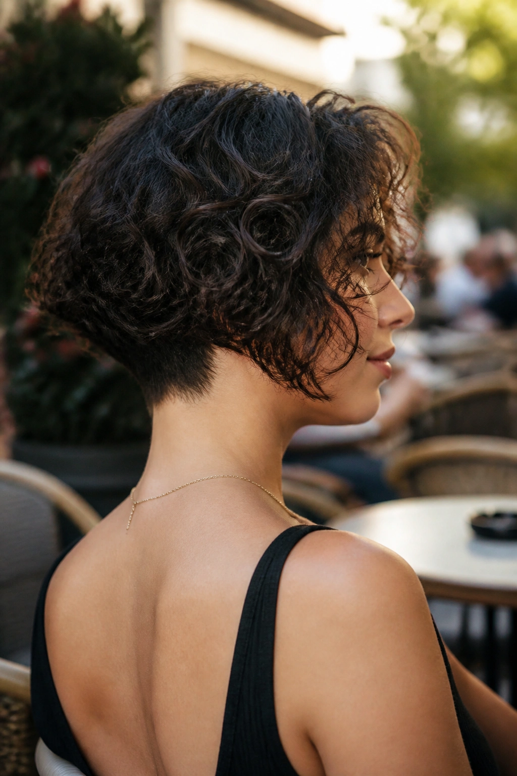 Medium-close portrait of a woman with an inverted curly bob and slim nape in natural daylight