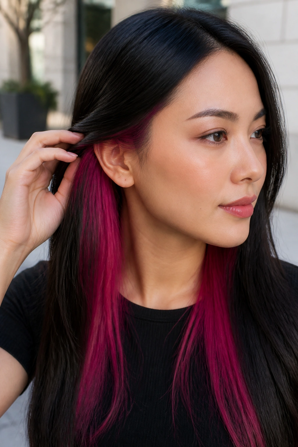 Close-up portrait of a woman with magenta underlayers peeking from beneath straight black hair.