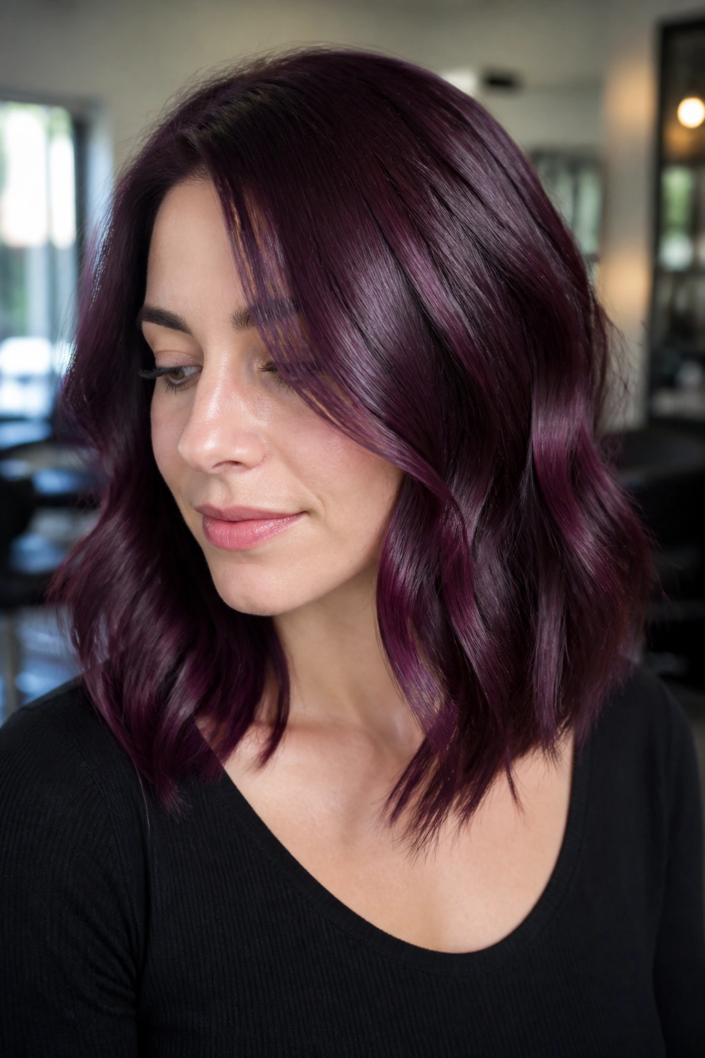 Close-up portrait of a woman with mulberry gloss hair in a softly lit salon.