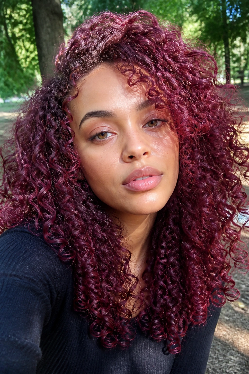 Close-up of real woman with mulberry pink curls in a park setting