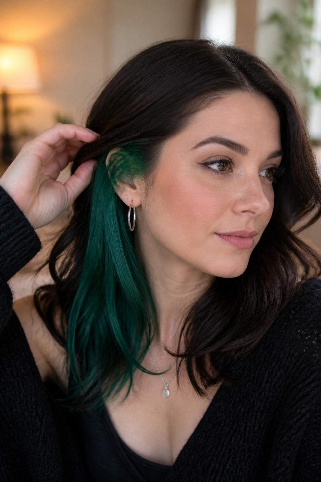Portrait of a real person with peekaboo emerald underlayers visible when hair is tucked behind the ear.