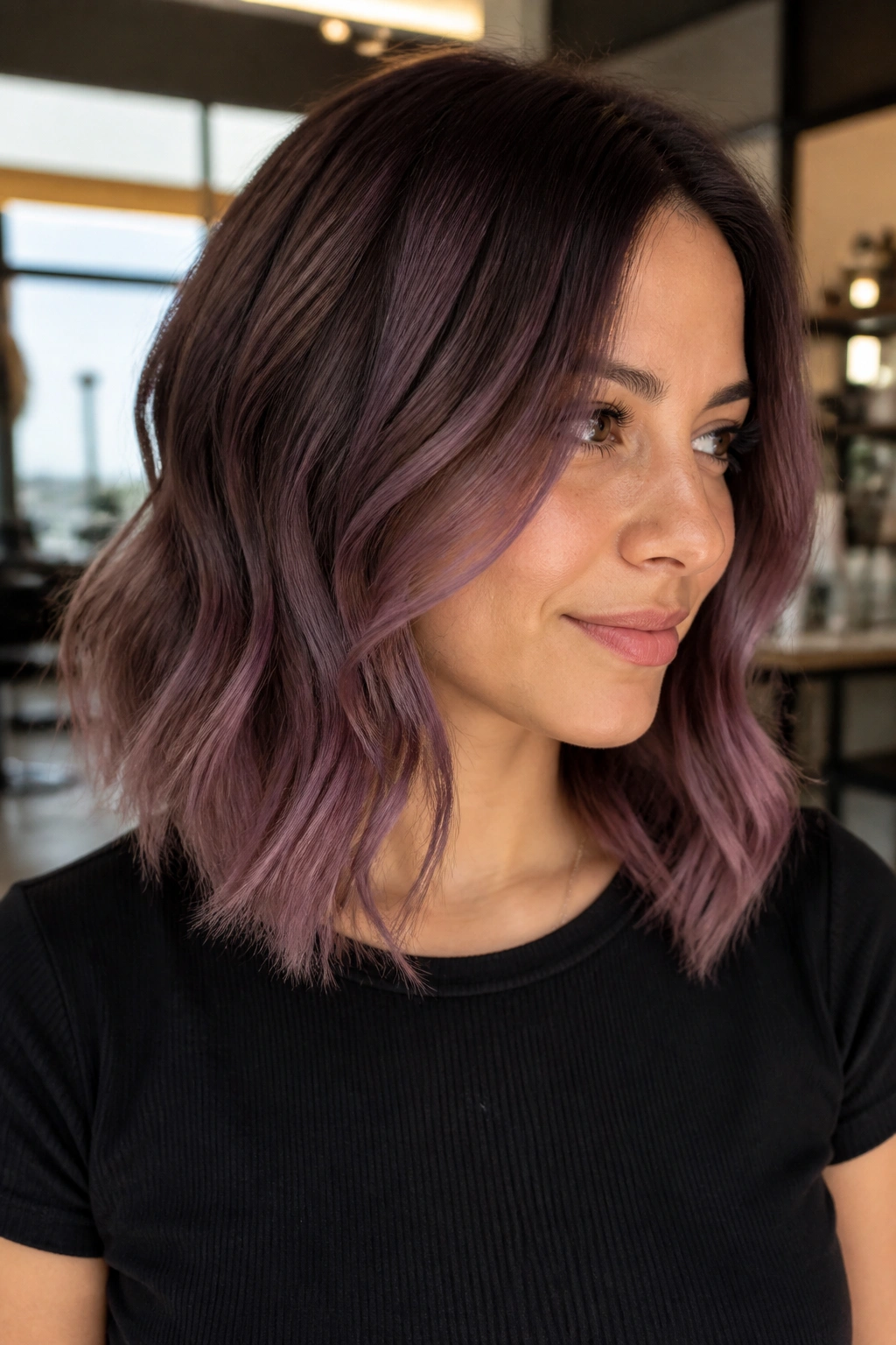 Close-up portrait of a real woman with purple brown shadow root and mauve mid-lengths in a warm salon
