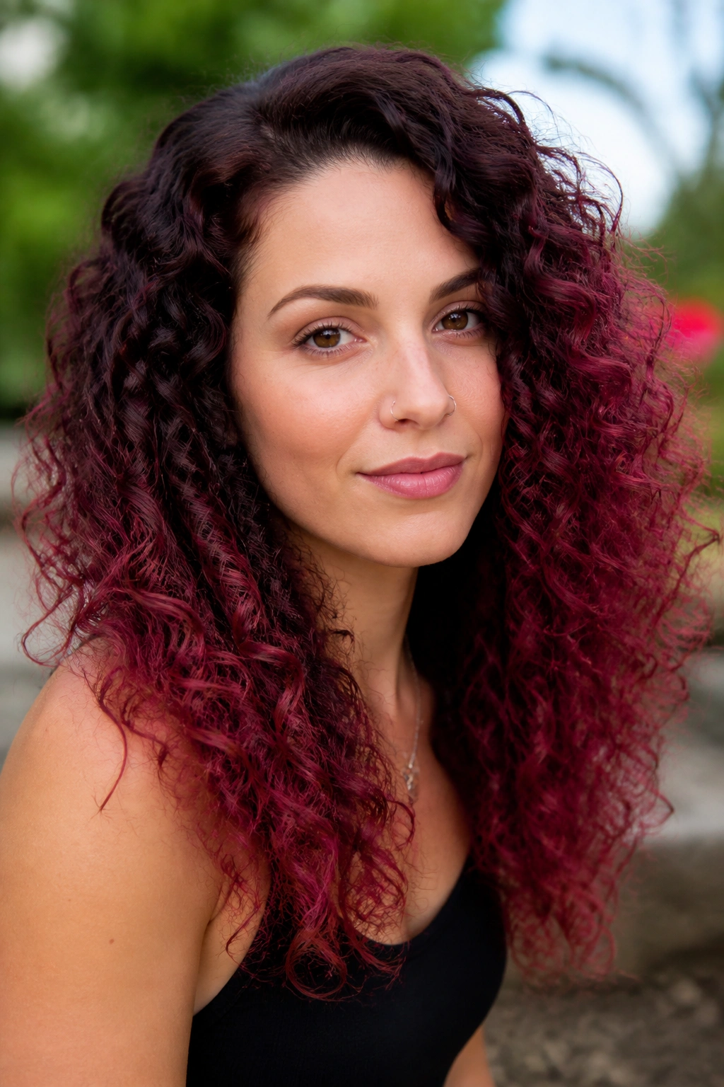 Portrait of a woman with raspberry ombré curly hair.