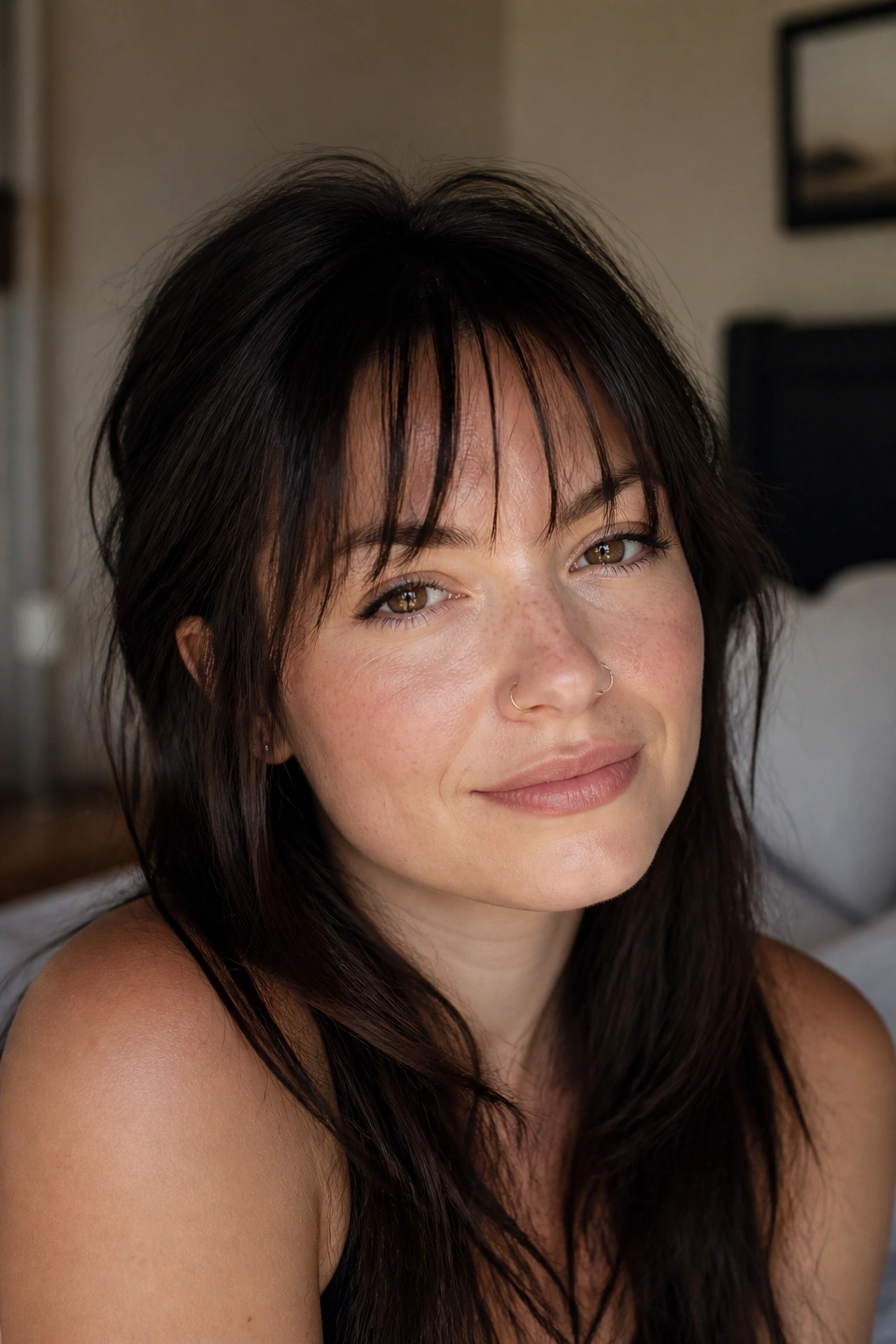 Close-up of a real woman with a piecey razor-cut fringe showing airy separation between strands in a bedroom