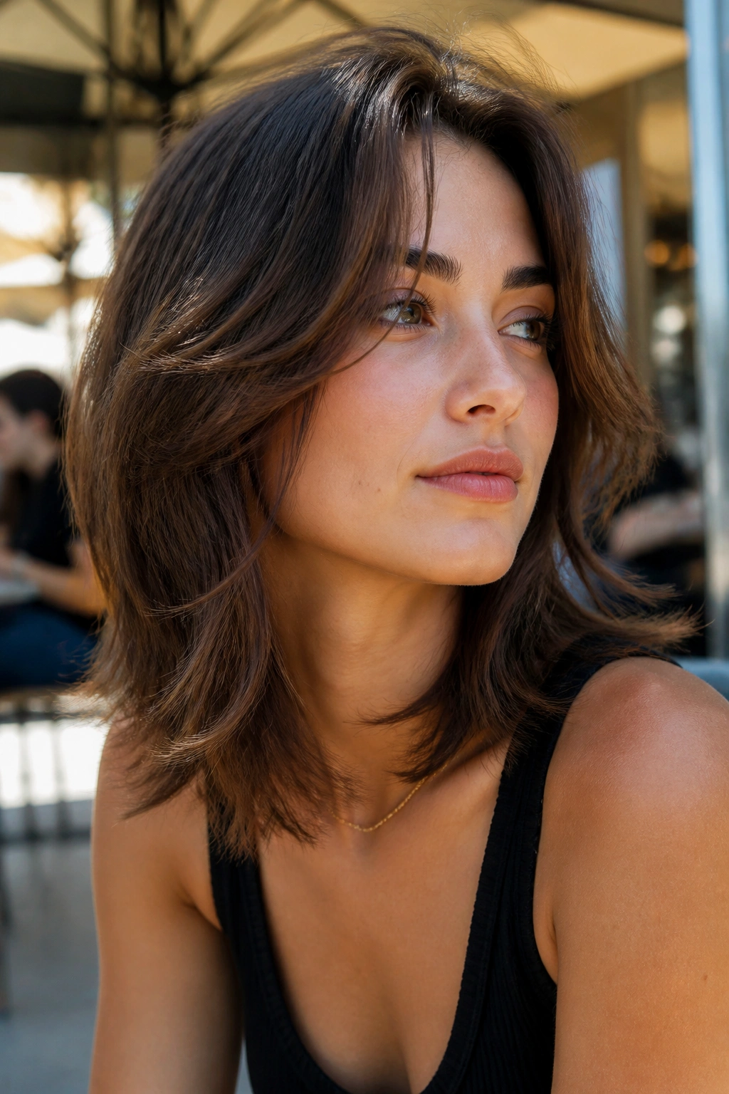 Close-up of a real person with razor-cut mid-length layers in natural daylight at an outdoor cafe