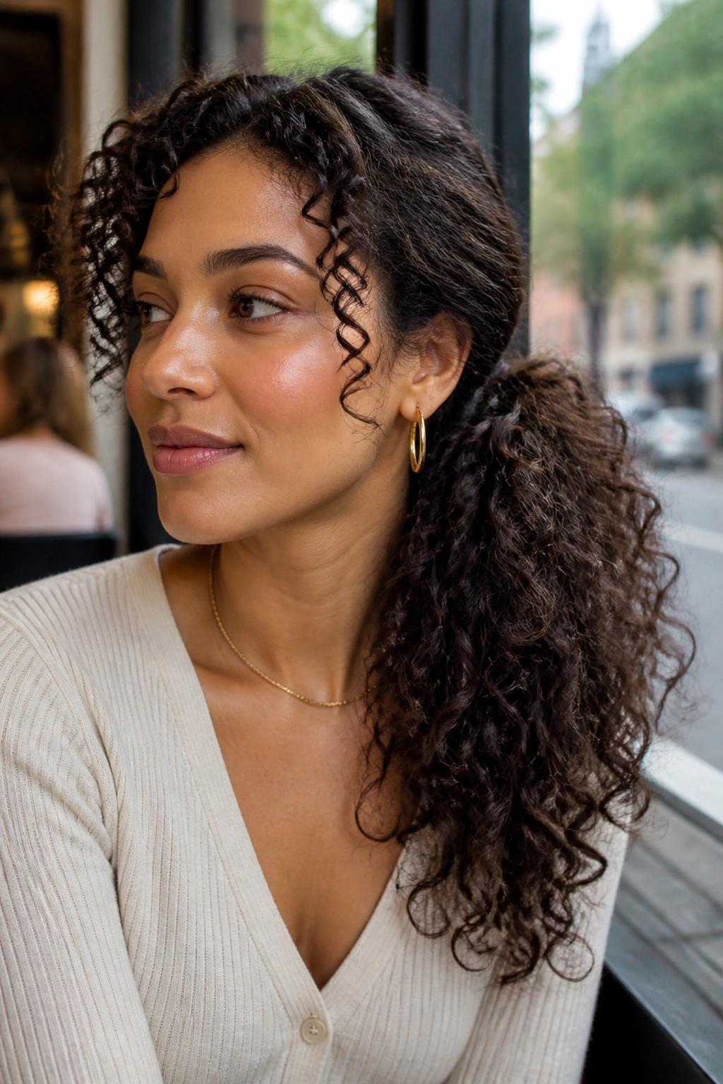 Close-up of a real woman with a side-swept curly ponytail in a cafe setting.