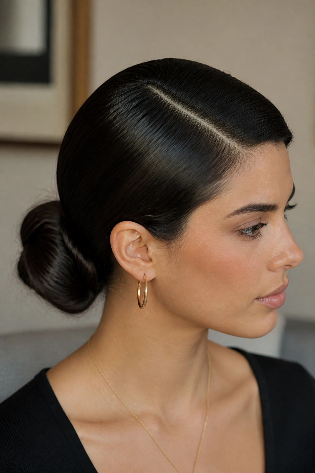 Close-up of a person with a sleek low bun and side part in thick, glossy waves