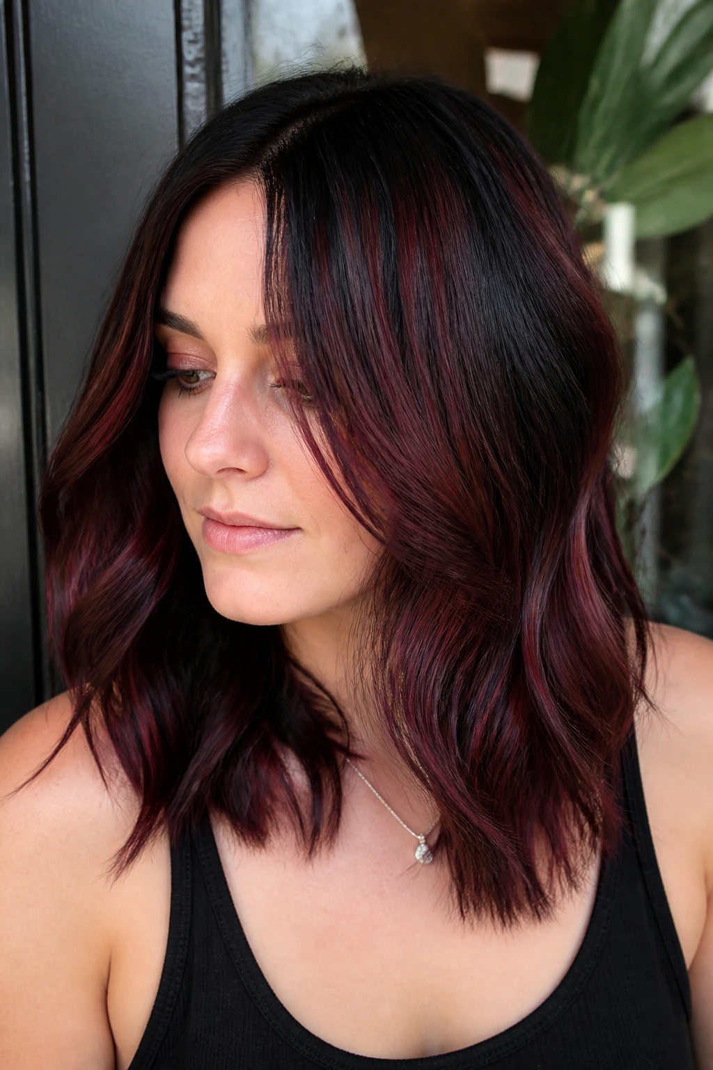 Real woman with smoky ruby layered hair catching light.