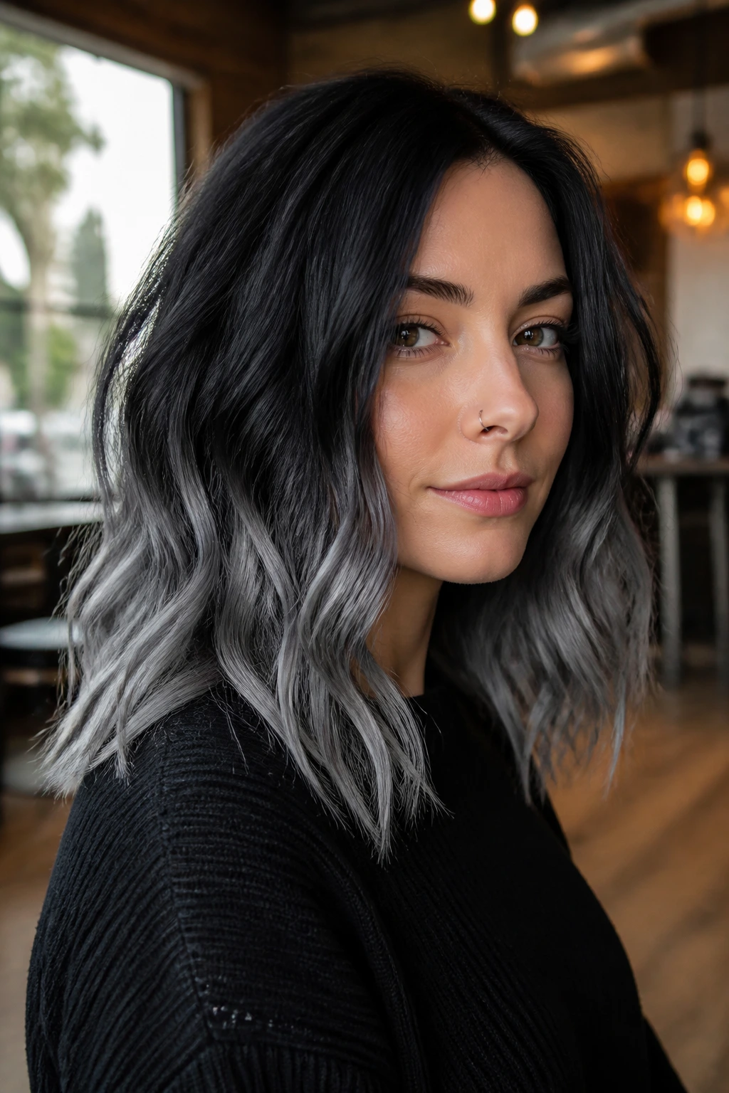 Close-up portrait of a real woman showing smoky gray dip-dye at the ends with black roots in a warm salon.