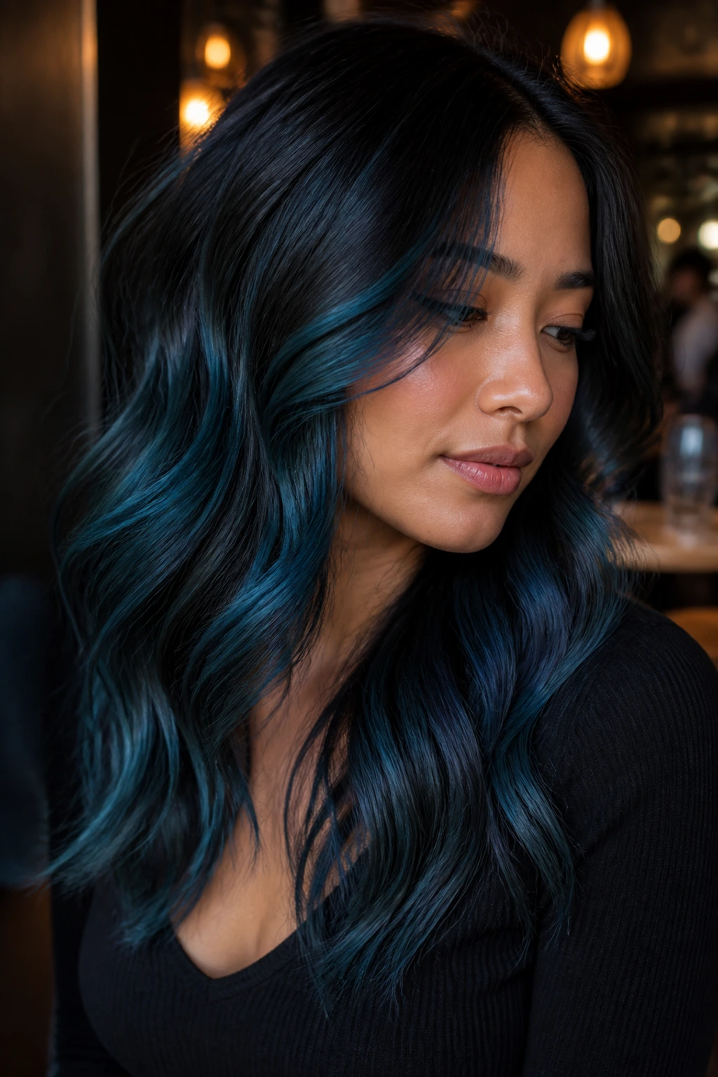 Close-up of dark brunette with smoky teal-blue balayage under restaurant lights