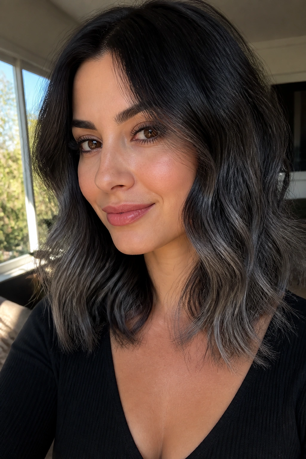 Close-up of a real woman with soft charcoal melt hair from black roots to grey ends in a sunlit living room