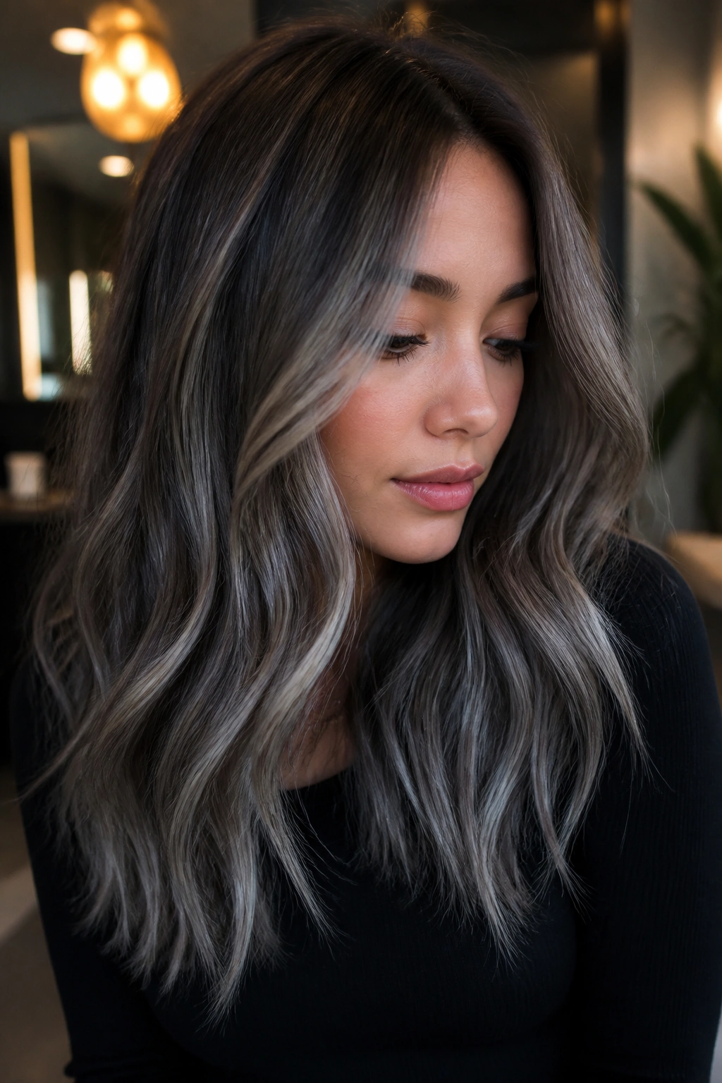 Close-up of a real woman showing steel-grey balayage on cool-toned brown hair in a chic salon.