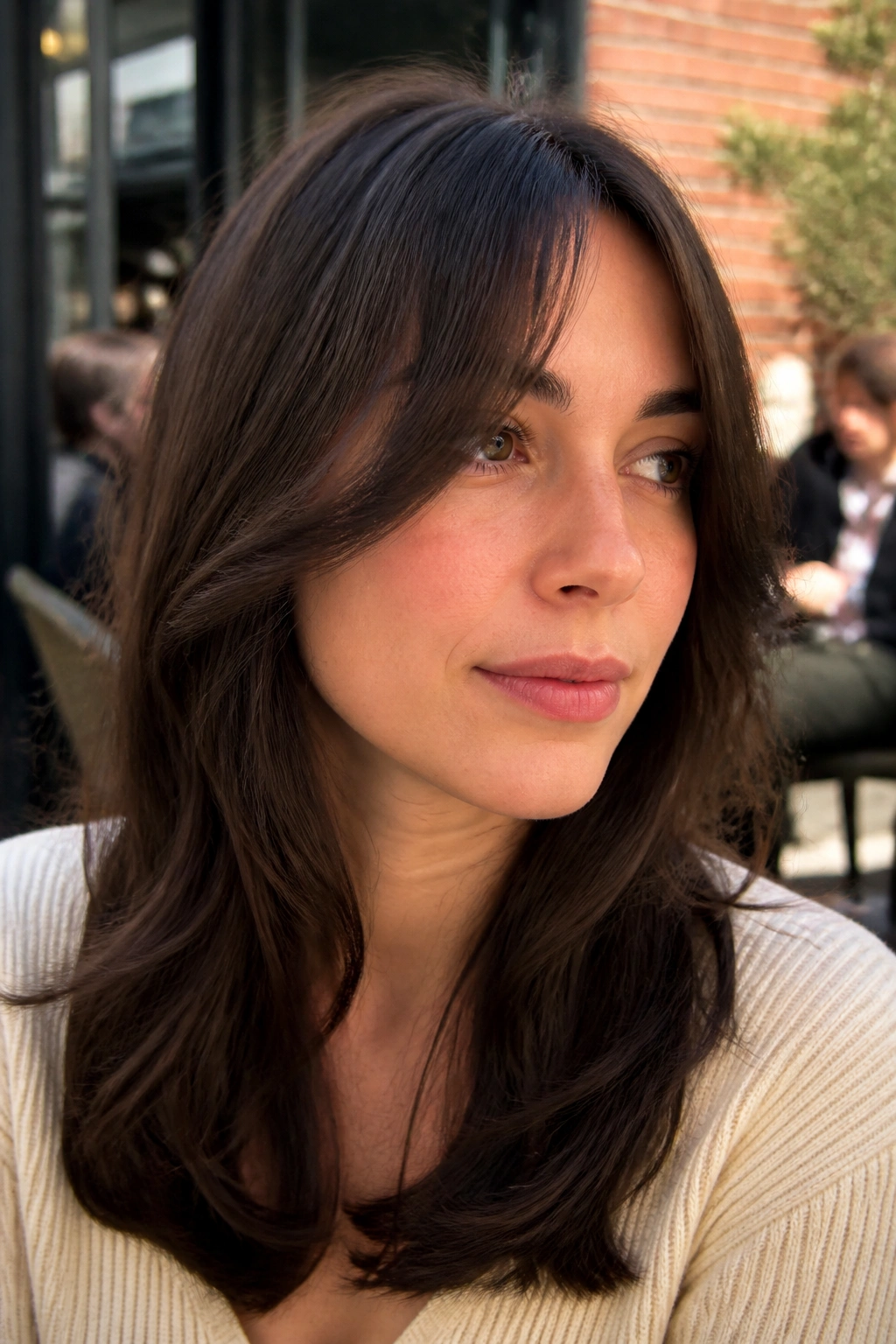 Close-up of a real woman with temple-sweeping half bangs outdoors at a cafe