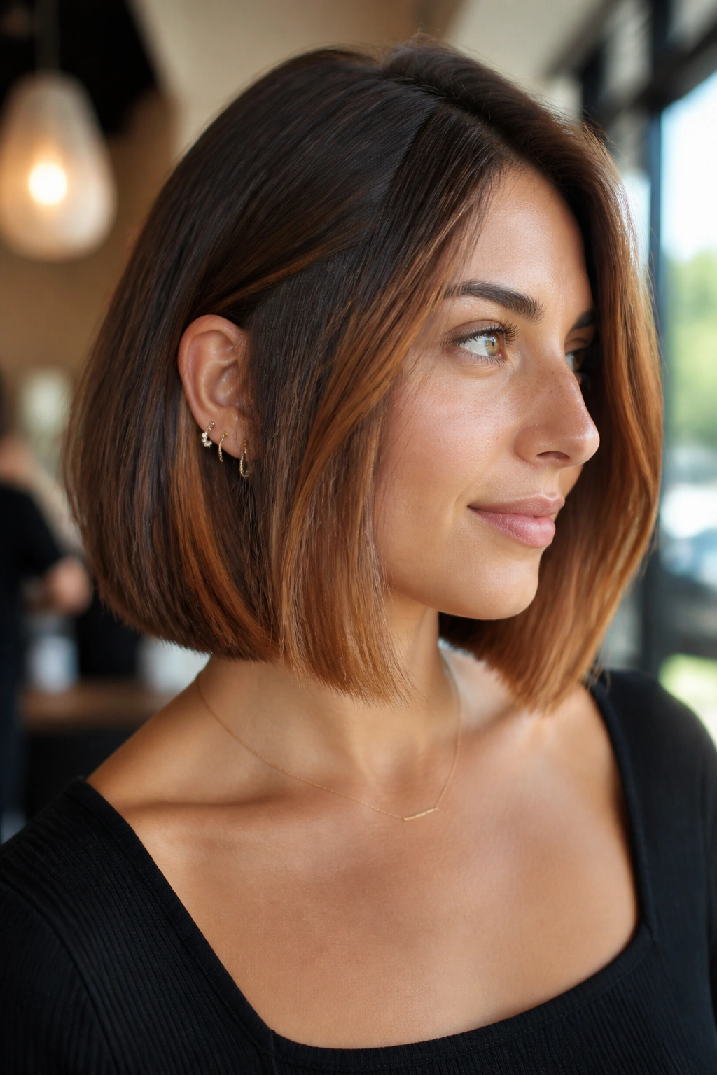 Close-up of a real woman with a blunt bob featuring toasted copper balayage in a warm salon setting.
