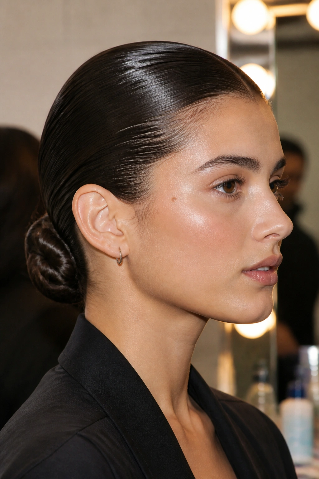 Close-up of a woman with a glossy wet-look low bun at the nape.