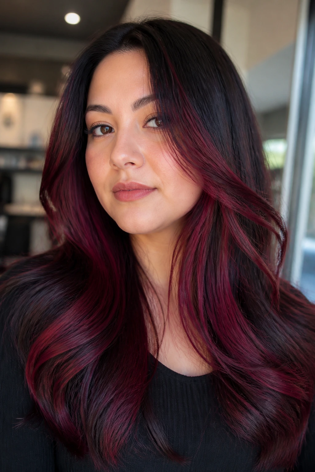 Close-up portrait of a real woman with wine red peekaboo layers under a top layer in a salon setting